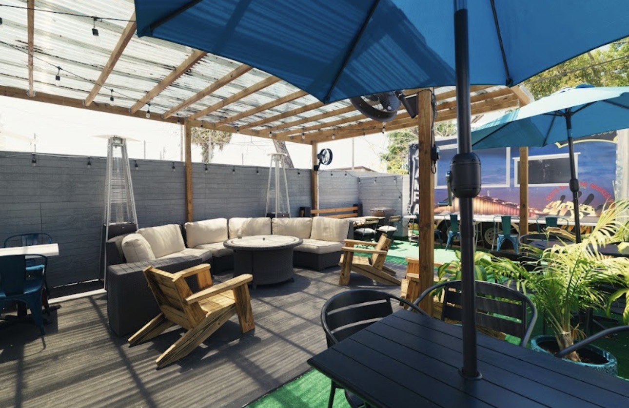 Noble Brew's covered outdoor patio with lounge seating, string lights, and shade umbrellas